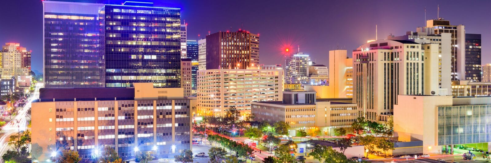 Lights from the towering buildings glow in the night at the streets buzz with light and activity in downtown San Diego