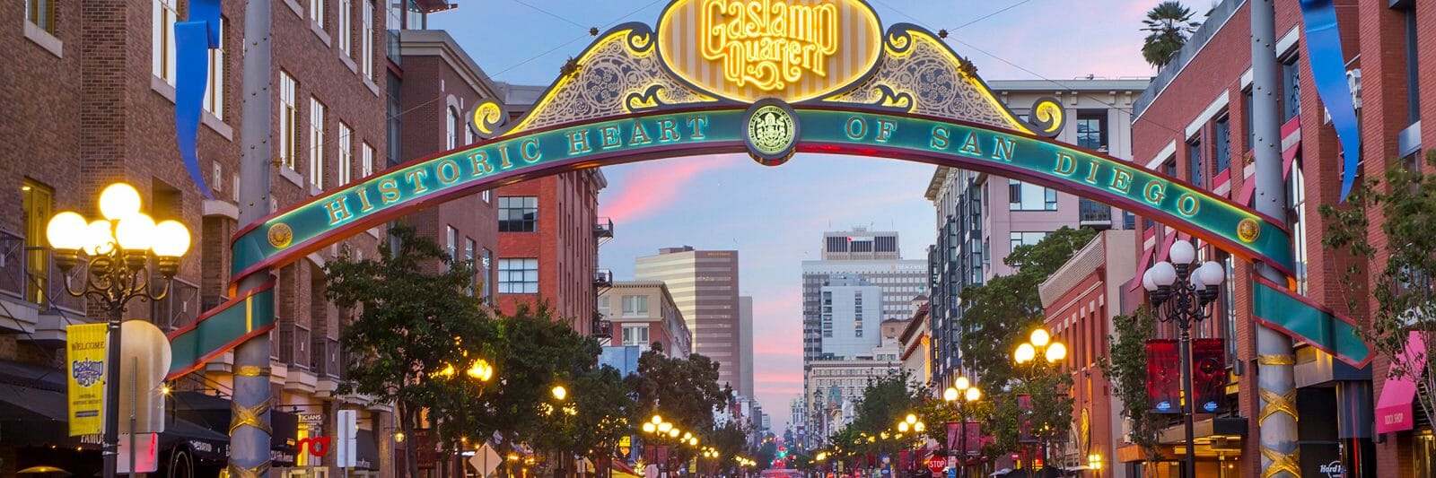 As the sun sets, cars zoom underneath the lit sign reading Gaslamp District in San Diego, California
