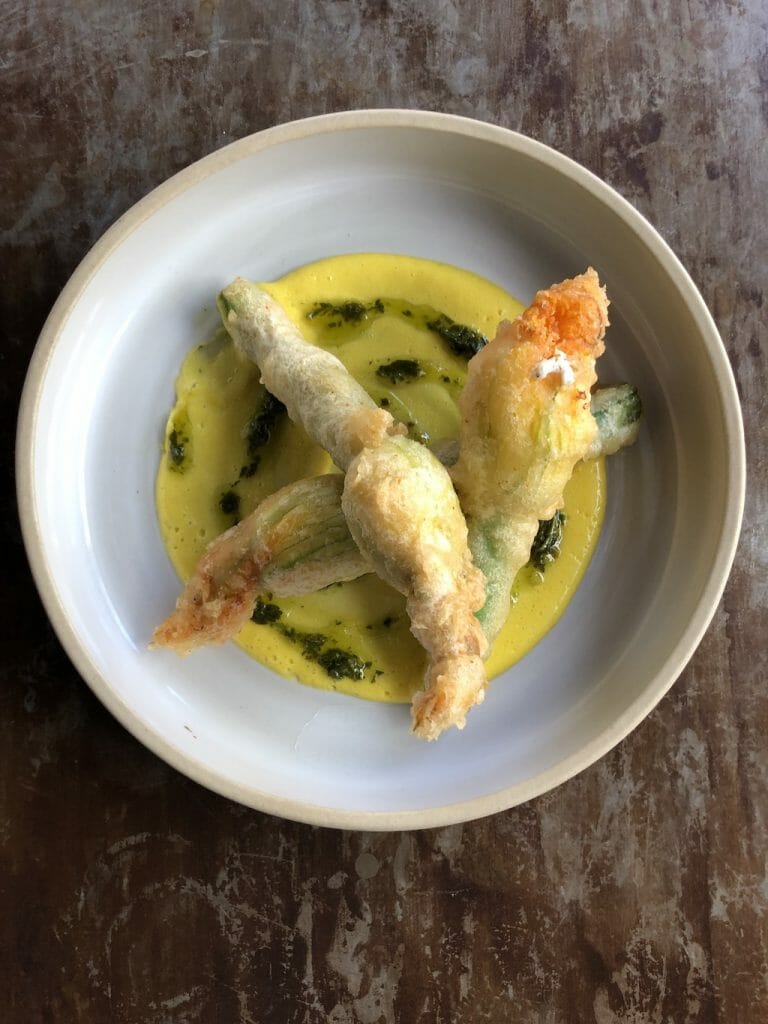 Perfectly fried squash blossoms sitting in a yellow sauce swirled with a black sauce