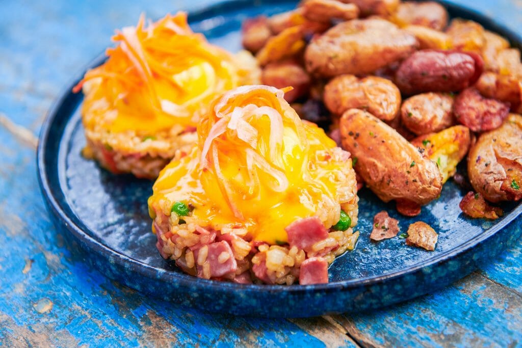 Two small piles of fried rice with two poached eggs and hollandaise on top. Potatoes and a radish salad garnish the place