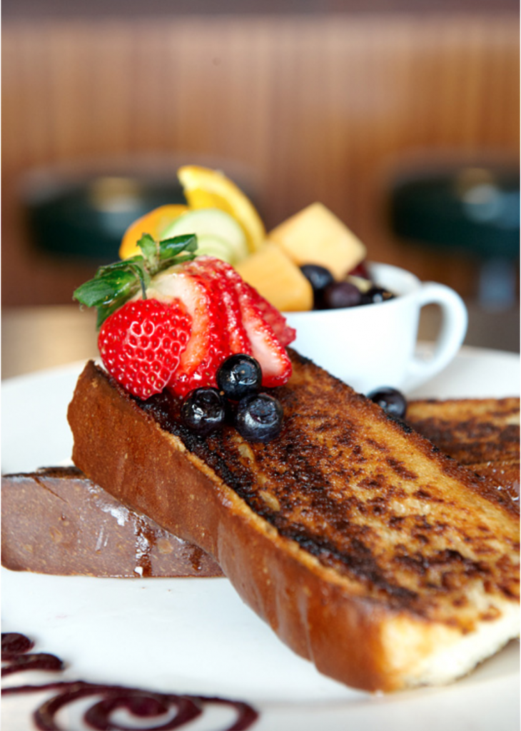 French toast topped with blueberries and strawberries with a fruit cup in the background