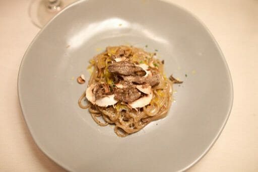 In a small pile, there is pasta, cheese, mushrooms, and cured egg yolk