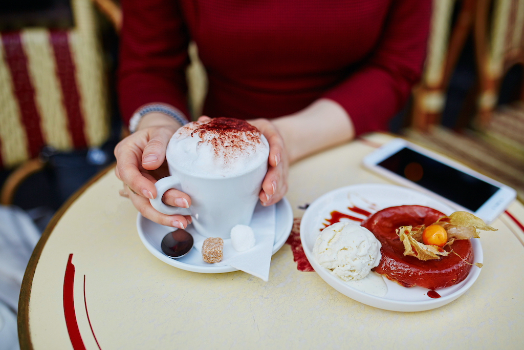 French woman drinking coffee in outdoor cafe in Paris, France and using her mobile phone for texting, browsing or photo. Closeup of hands holding gadget