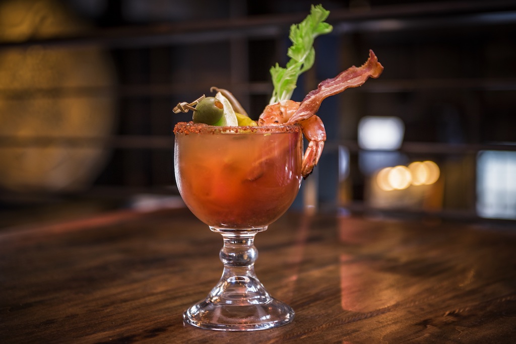 In a clear goblet, a bloody mary is garnished with bacon and celery