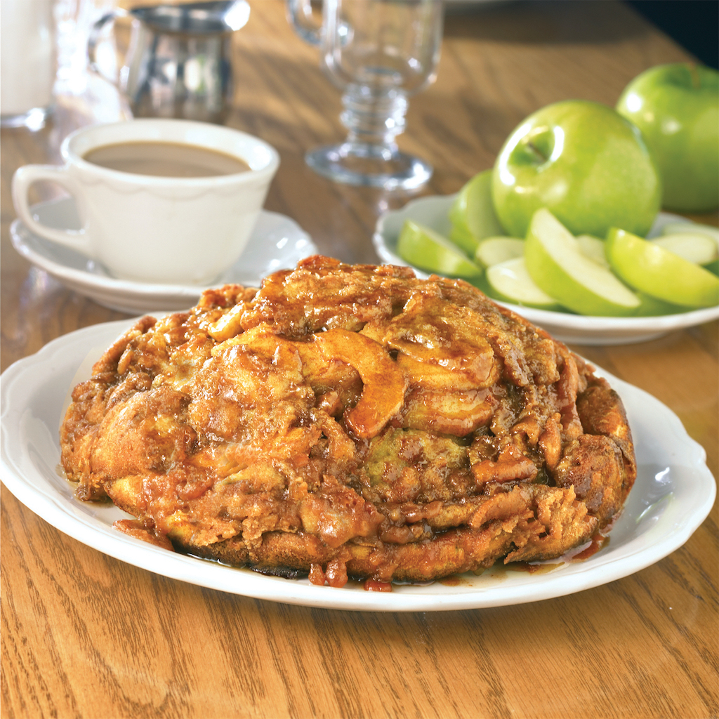 A big lump of a pancake filled with apples and sugar laid on a plate near coffee and whole apples