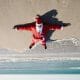 inverted image of santa claus lying face up on the sand of a beach, with the sea in the background