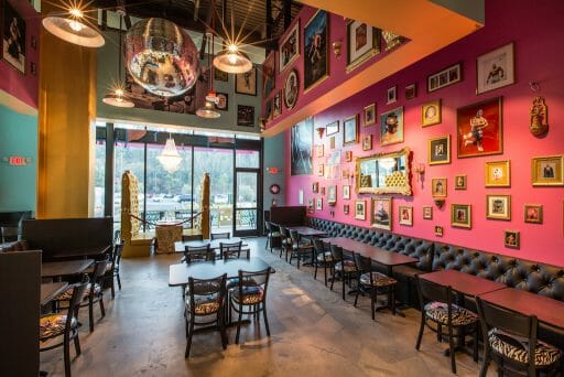 A pink wall vibrantly decorated with photos as chandeliers dangle from the ceiling as natural light also shines through