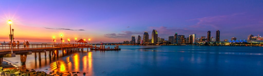 Panorama of Coronado old pier reflecting on in San Diego Bay from Coronado Island, California, USA. San Diego cityscape skyline with Downtown and Waterfront Marina District at twilight on background.