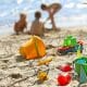 colorful beach toys and buckets laying in the sand with three kids playing on the beach in the background