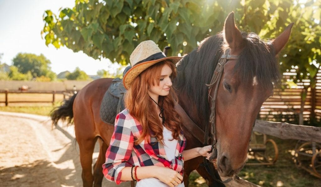 Red haired woman leading a brown horse on a horse farm