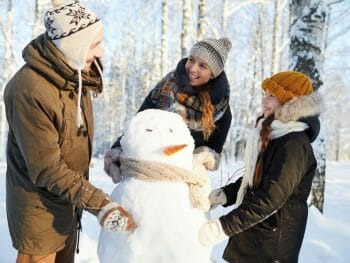 Family with one kid building a snow man in a wintery landscape