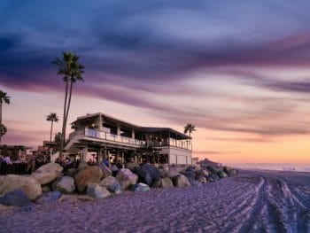 View of two story building right on the beach during sunset photographed from the beach - home to Pacific Coast Grill
