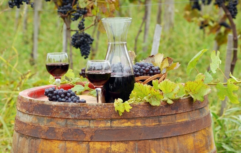 Old rustic wine barrel in a vineyard with wine glasses and bottles and grapes on top - Temecula Red Wines