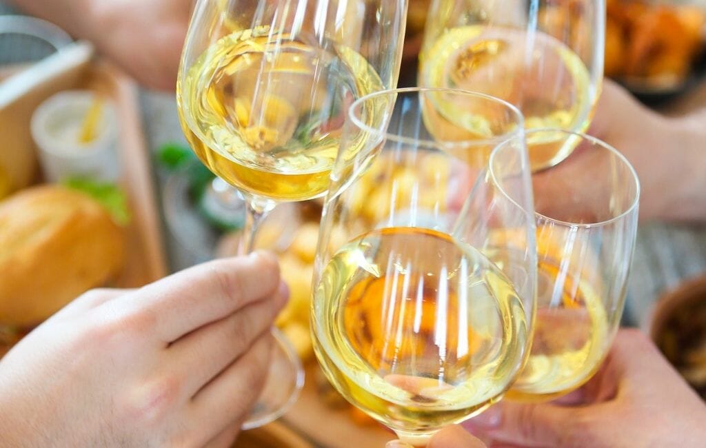 4 white wine glasses with hands toasting with each other