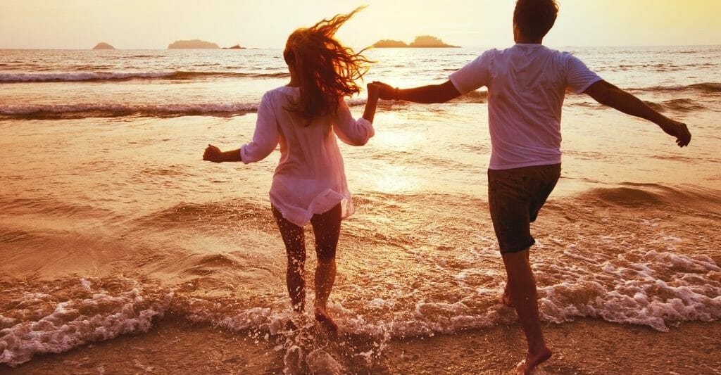 young couple running into the shallow water on the beach during sunset while holding hands