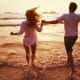 young couple running into the shallow water on the beach during sunset while holding hands