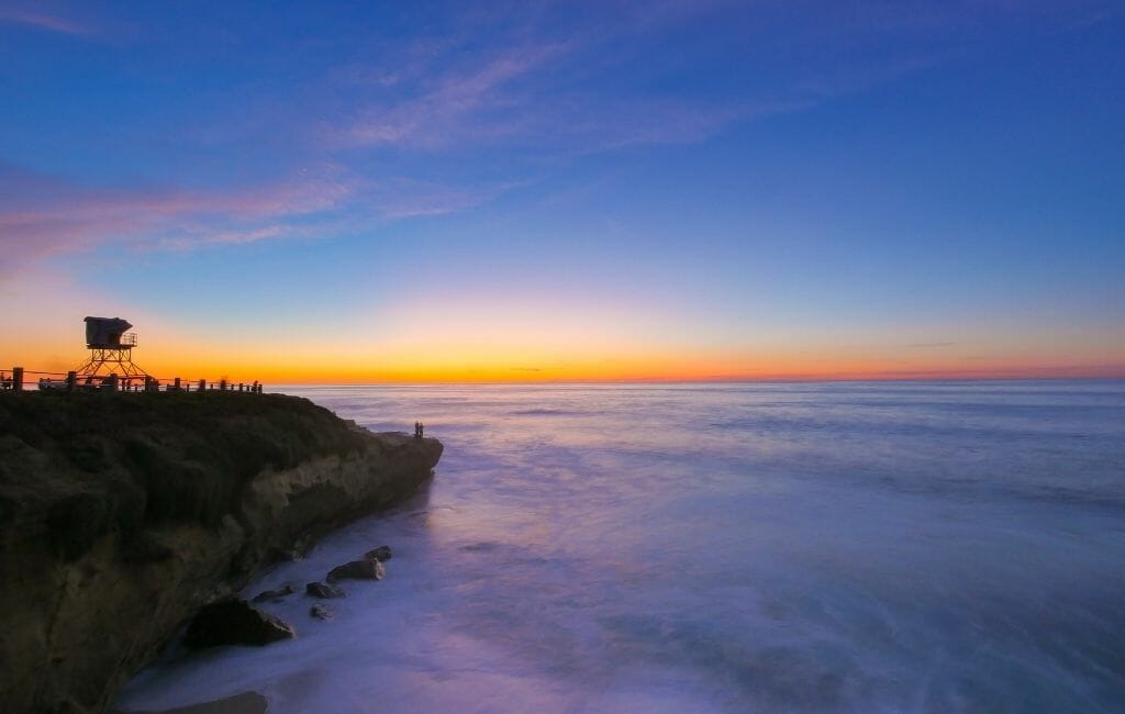 sunset over the pacific in La Jolla with sandstone cliffs on the left with a lifeguard tower on top