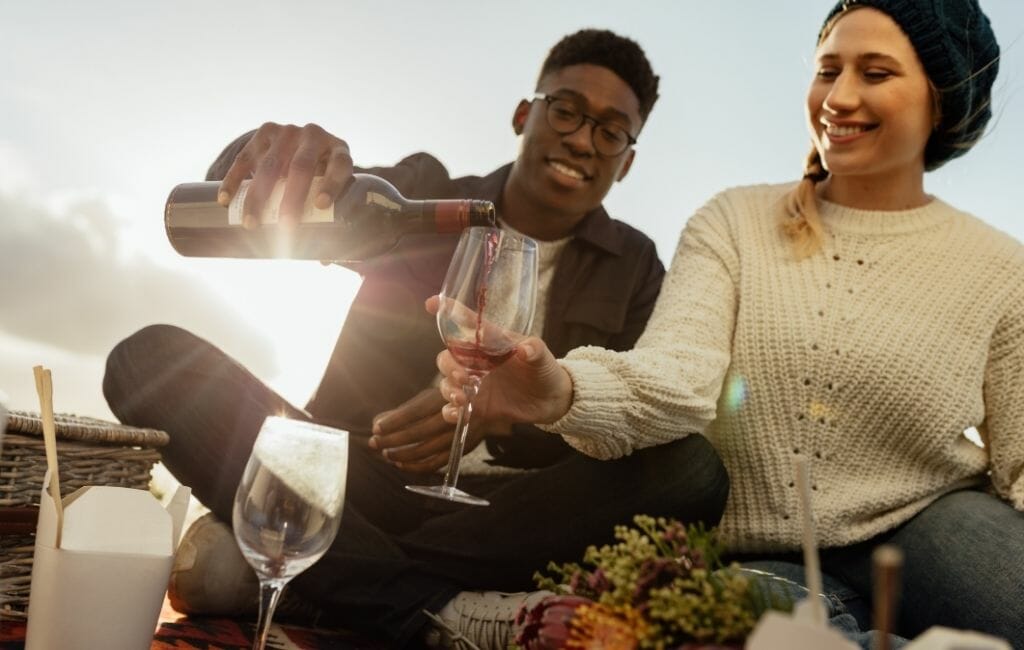 young couple having a picnic, man pouring wine for woman
