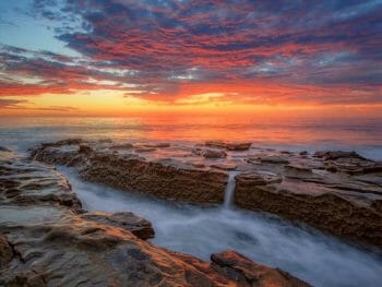 Long exposure sunset photo on Windandsea beach with water flowing over rock formation during colorful sunset