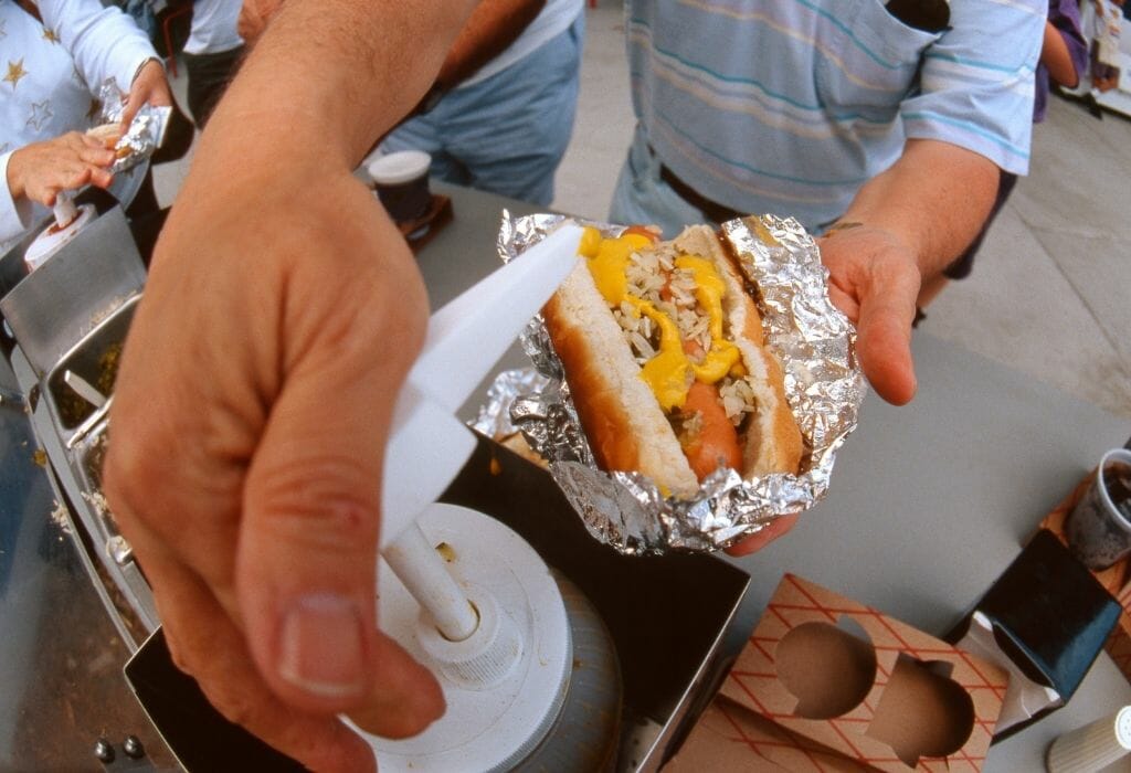 Closeup of a man's hand pumping mustard on a hot dog at a baseball ballgame