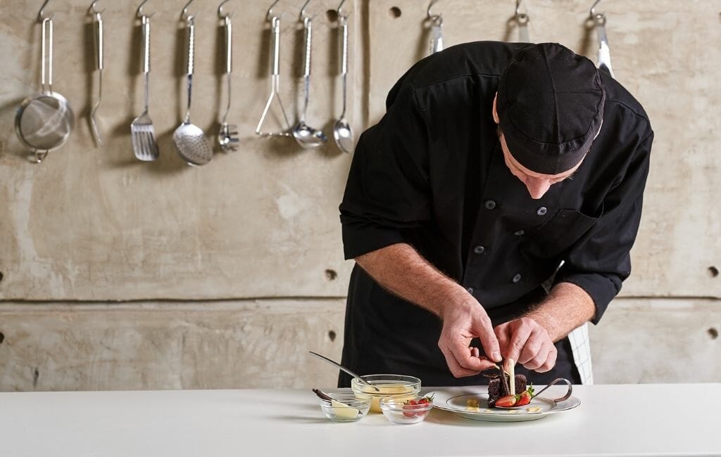 Chef in black uniform plating a plate in a modern kitchen - San Diego Restaurant Week