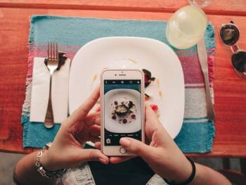 two female hands taking photo of plate of food on a colorful table setting