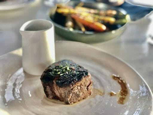 Filet Mignon Steak on a white plate with a small saucier and bowl with carrots in the background