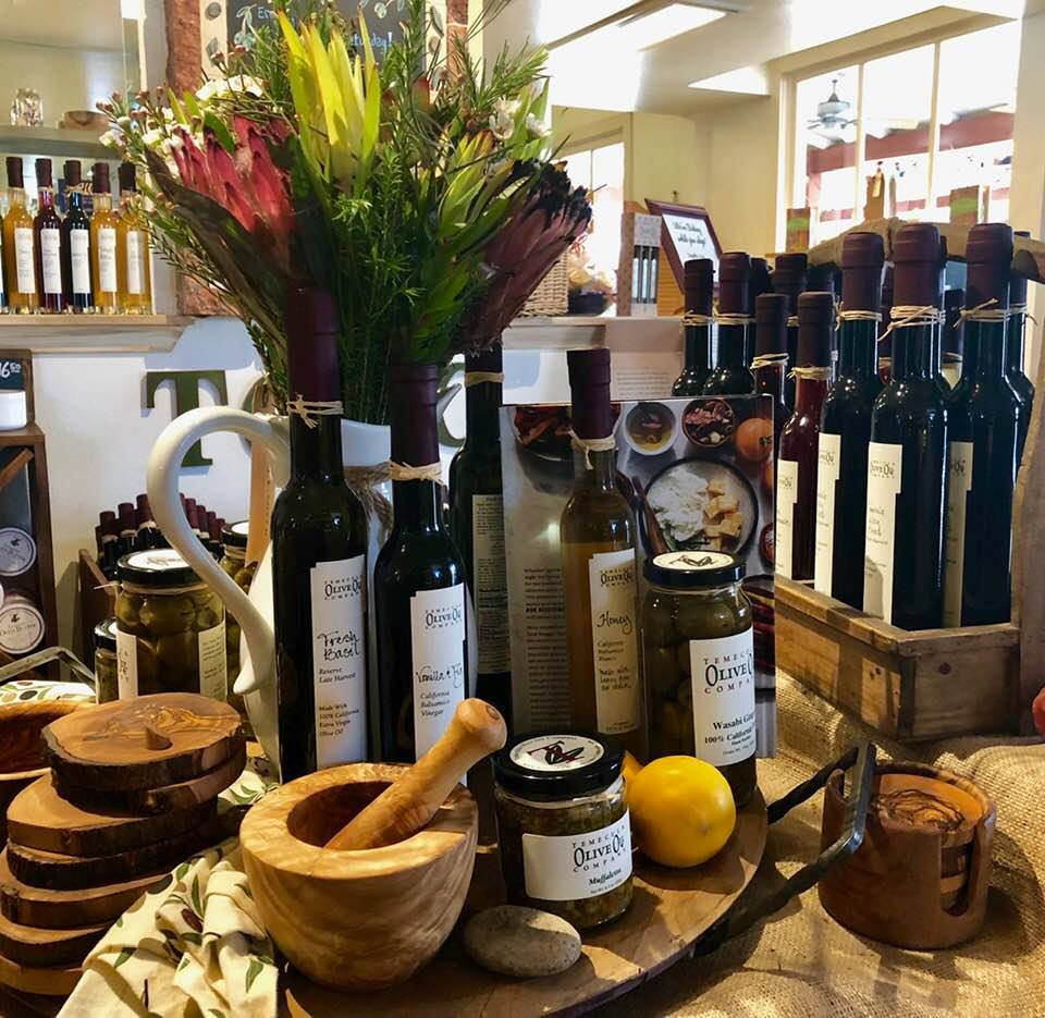 Table at the shop at Temecula Olive Oil Company with various olive oils, spreads, mortar and pestal, and flowers - Things to do in Temecula