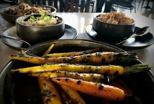 yellow and orange carrots with grill marks and parsley spinkled on top in a dark ceramic bowl