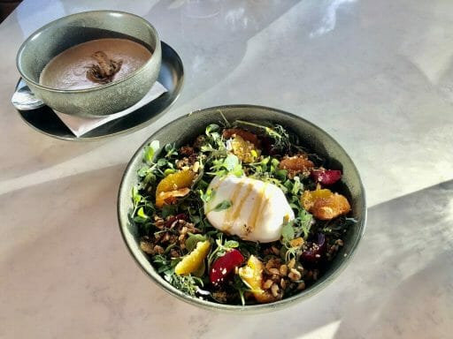 quinoa salad with oranges and beets and a large burrata cheese in the center and a bowl of mushroom soup in the background (blurred)