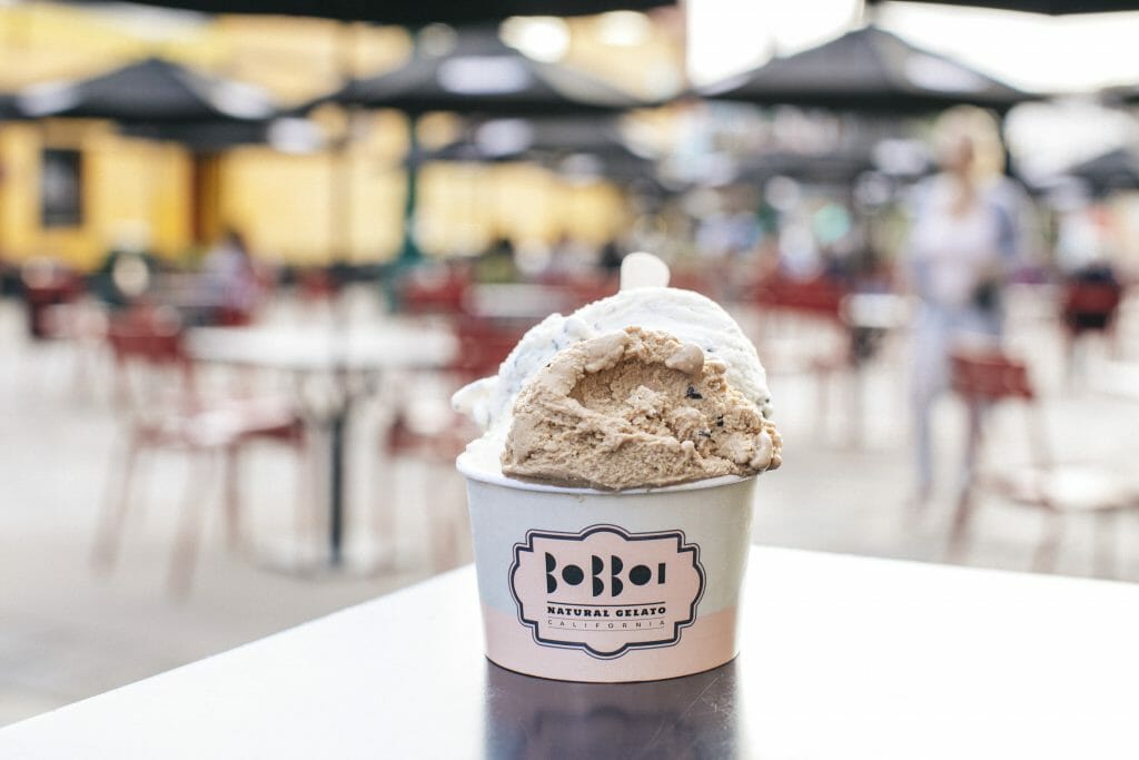 A paper bowl of light brown gelato on a table with the Piazza della Famiglia in the background -Bobboi Gelato - Photo by Diana Rose Photography