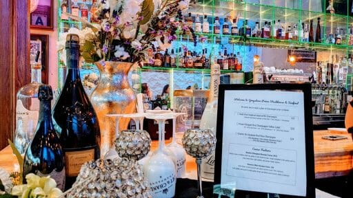decorated table with champagne bottles, flowers, menu and glasses in front of mirrored bar