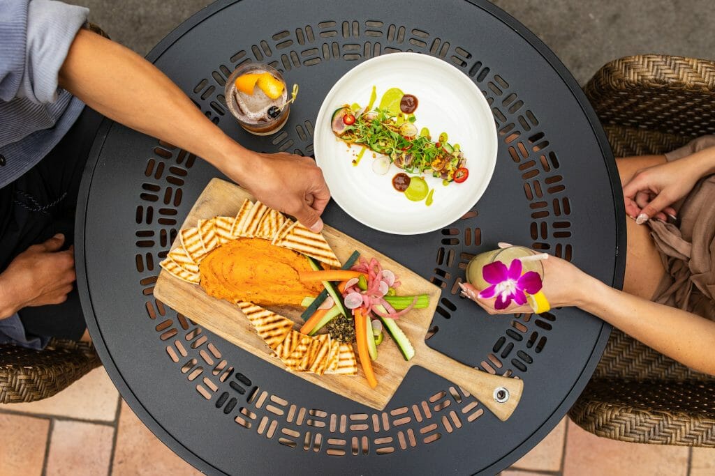Flatlay of table with various plates and foods with a male and female hand reaching in