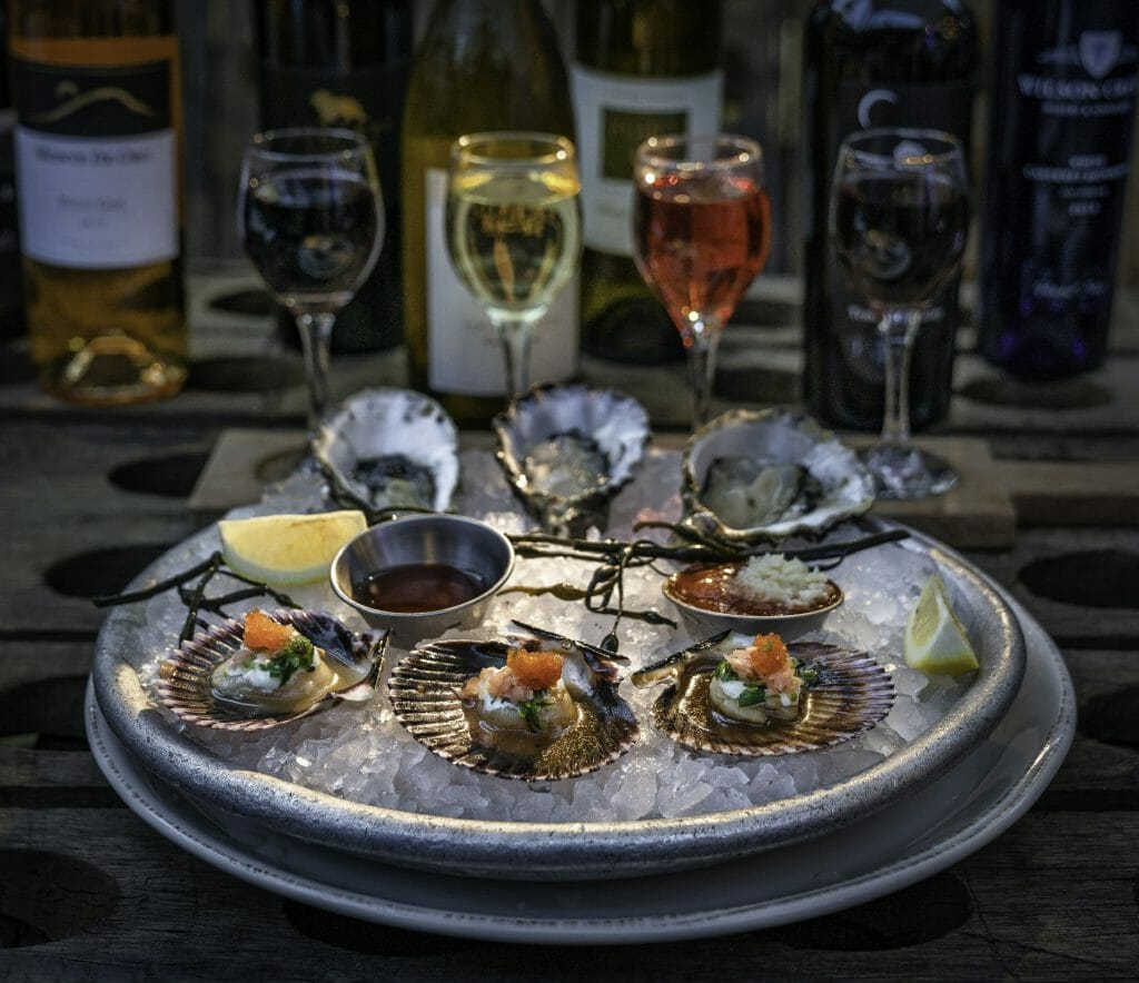 Metal plate with ice topped with clams and selection of wines in the background at Bluewater Grill Temecula