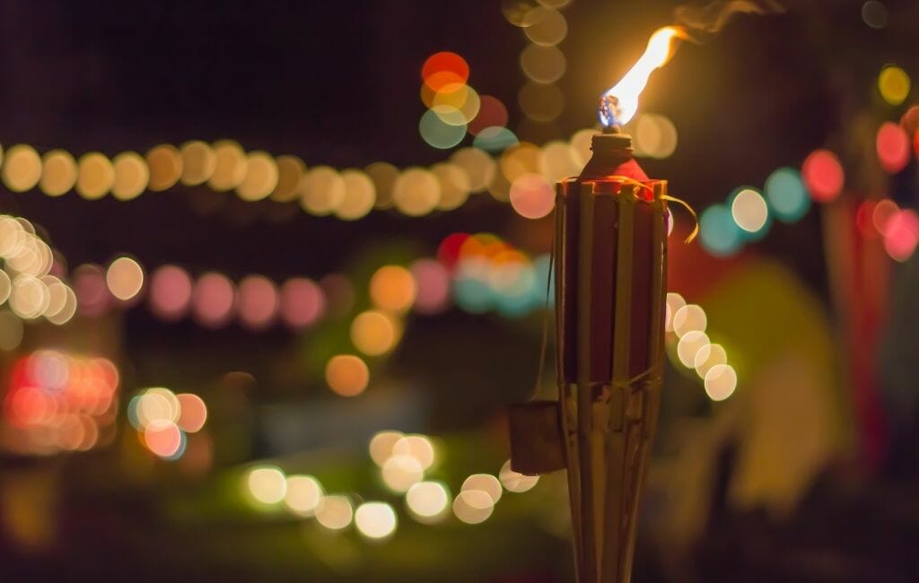 tiki torch in the foreground to the right, and colorful bokeh lights in the dark background