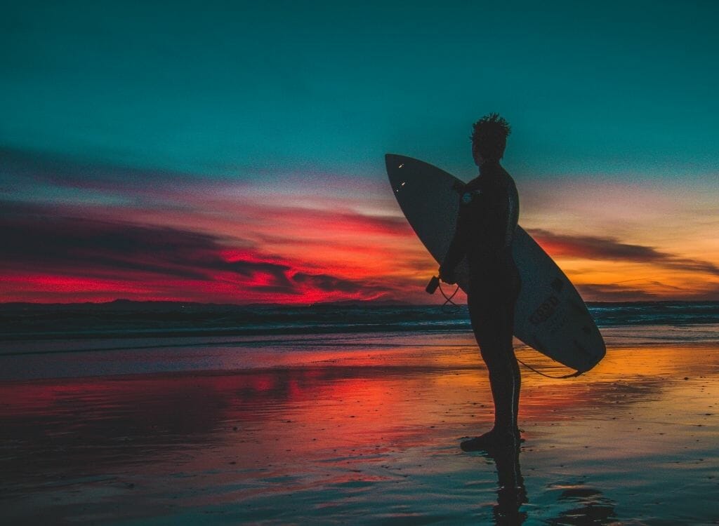 Silhouette of a surfer with surfboard during very colorful sunset