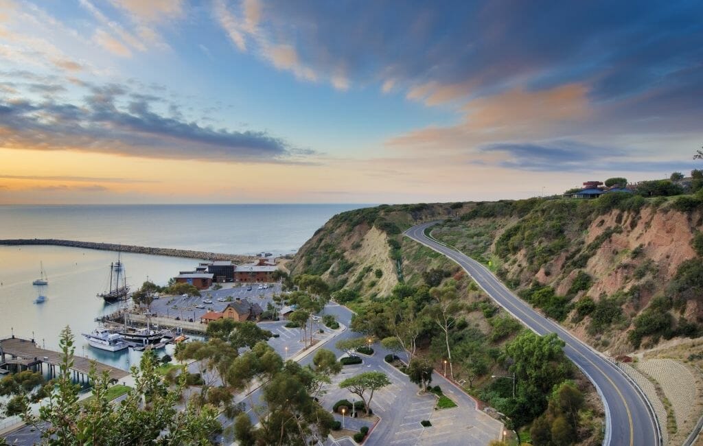 sunset over coast line near Dana Point Harbor with road on the right, harbor with sailboats and bridge on the left