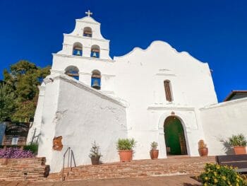 Mission San Diego Church - white Front with open bell tower with 5 bells, red brick walk way and dark blue sky
