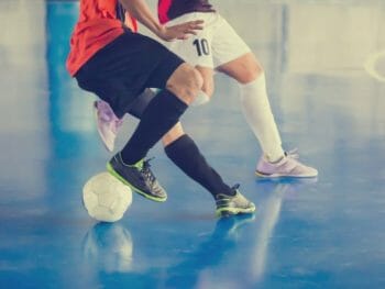 legs and lower torso of two male socker players indoors on blue surface