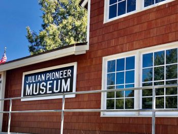 Red wood building with white trim and a black sign with white letters: Julian Pioneer Museum