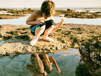 Boy looking at tide pools on rocky ocean shoreline. San Diego tide pools. Tide pools San Diego.