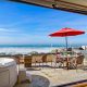 Outdoor deck with dining table and hot tub overlooking Pacific Ocean on sunny day.