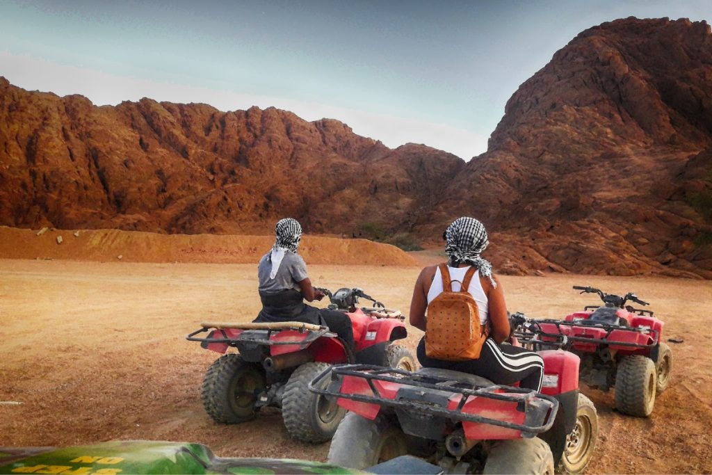 2 atvs with riders from the back, with desert landscape in the backgrund