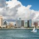 Small sailboat sailing calm waters with San Diego skyline in background on sunny day. Sailboat tours San Diego.