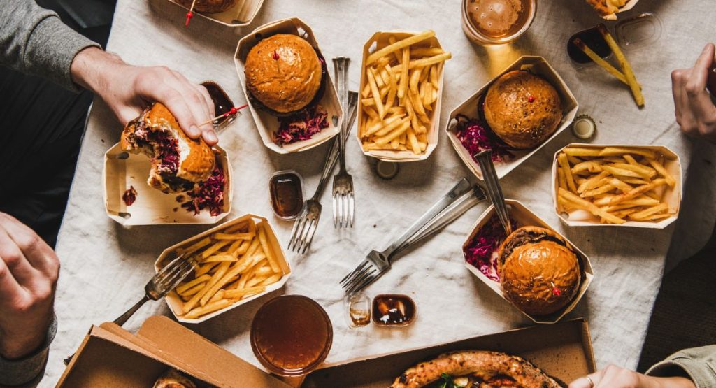People around table covered in hamburgers, french fries, and pizza. San Diego Food Tours.