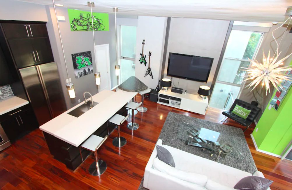 Kitchen and living room with modern furnishings, dark wood floors, neat kitchen, and bright green pops of color with accent wall and decor.