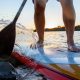 Close up action shot of man paddle boarding on calm water during sunset. Paddle board is colorful and water is splashing in the air has he paddles. SUP rentals in San Diego.