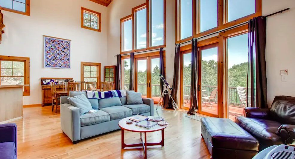 Spacious living room and dining room area with hard wood floors, cozy furniture, and floor to ceiling windows with mountain views.