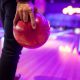 Close up of a man holding a red bowling ball in front of bowling lane, lit up with colorful lights at night. Bowling alley San Diego.