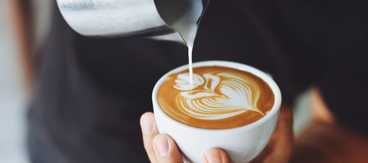 Close up of man pouring steamed milk into espresso creating a flower shape. Latte art, Coffee shops in La Jolla.
